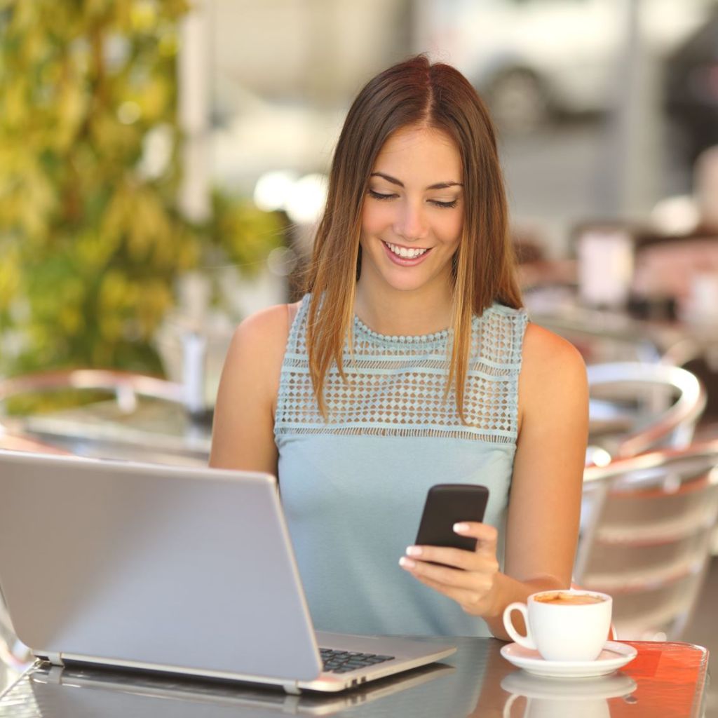 Frau nutzt Laptop und Smartphone in einem Café